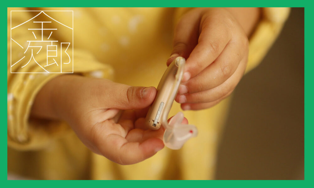 補聴器を持つ黄色い服を着た子供の手
