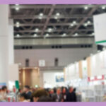大きな会場内で展示会が行われている。展示ブースが並んでおり、その間の通路に人が集まっている会場の様子