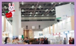 大きな会場内で展示会が行われている。展示ブースが並んでおり、その間の通路に人が集まっている会場の様子