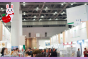 大きな会場内で展示会が行われている。展示ブースが並んでおり、その間の通路に人が集まっている会場の様子
