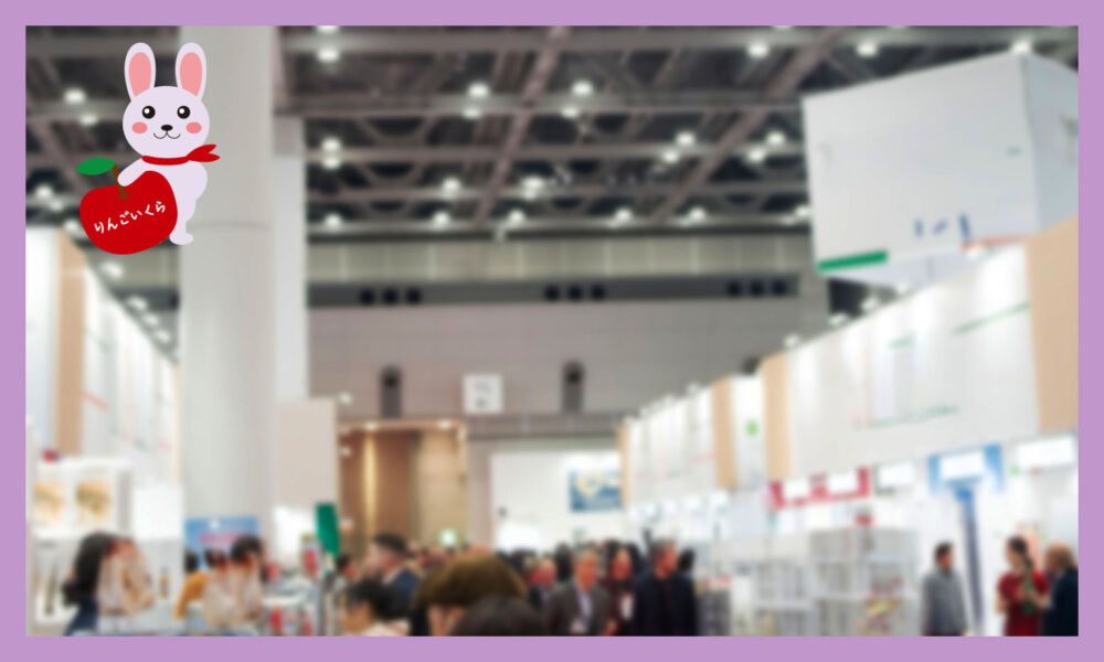 大きな会場内で展示会が行われている。展示ブースが並んでおり、その間の通路に人が集まっている会場の様子