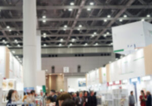 大きな会場内に展示会が行われている。展示ブースが並んでおり、その間の通路に人が集まっている会場の写真。