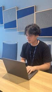 オフィスにて、黒いTシャツの男性がPCに向かって作業している