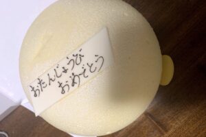丸い白い可愛いケーキに白いチョコが乗っている。そのチョコにおたんじょうびおめでとうと書いてある。
