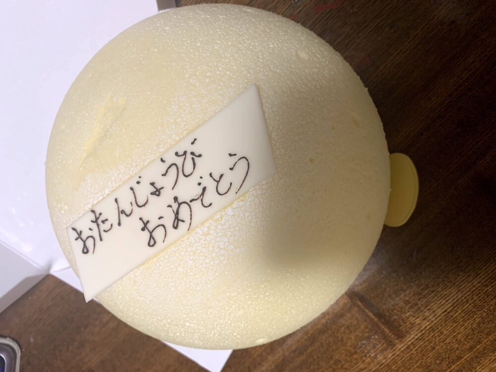 丸い白い可愛いケーキに白いチョコが乗っている。そのチョコにおたんじょうびおめでとうと書いてある。