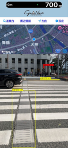 視覚支援アプリ「アイナビ」の画面。カメラで道路の横断歩道付近を映しており、画面上に横断歩道や点字ブロックなどの位置を示す黄色い枠や案内が表示されている。
