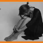 女性が顔を伏せて、膝を抱えて床に座っている画像